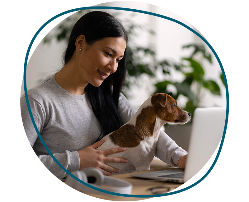 a woman in a gray sweater smiles while holding a small brown and white dog on her laptop